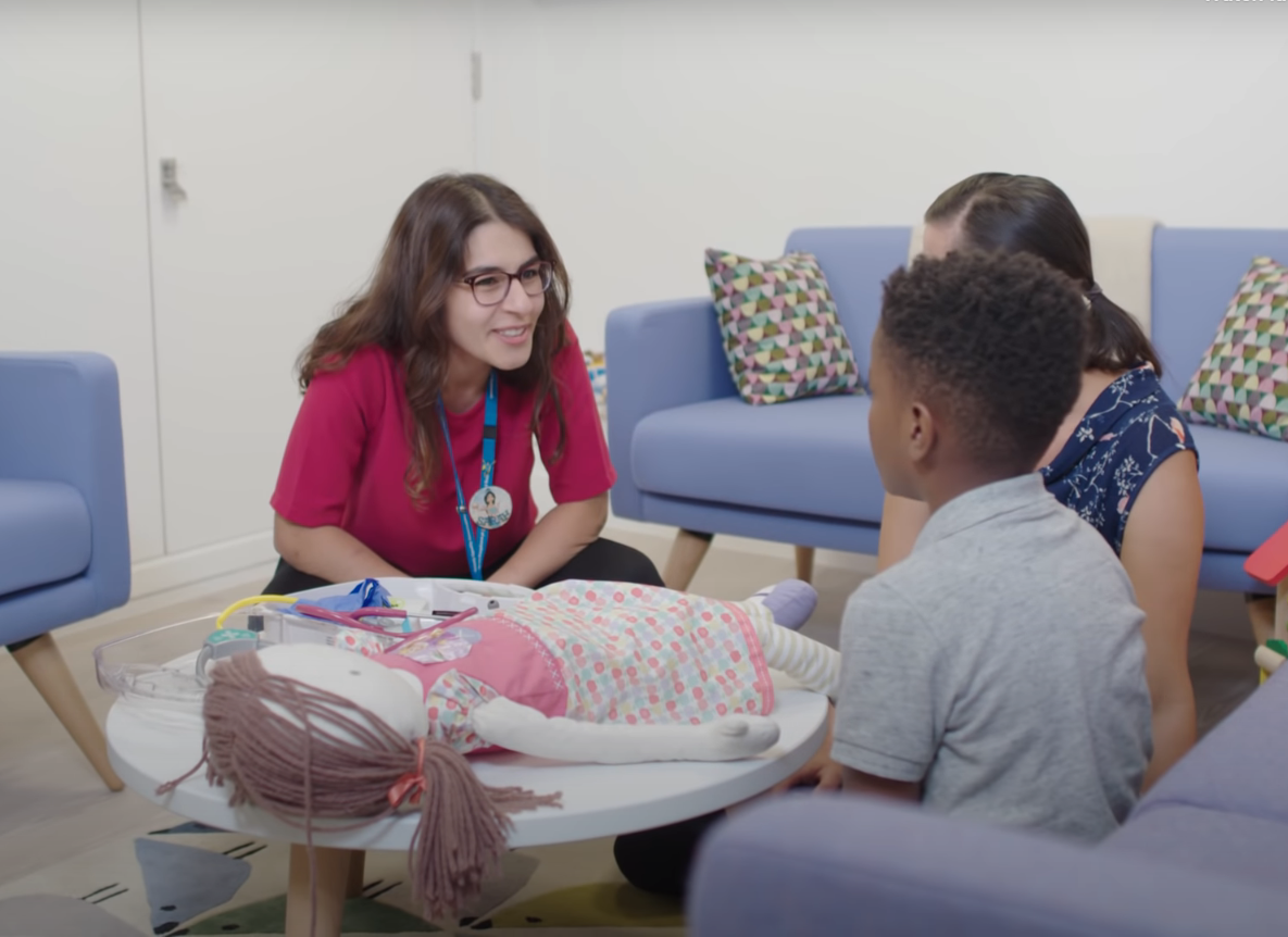 Female doctor speaks to a young boy and his mum, with toys in front of him