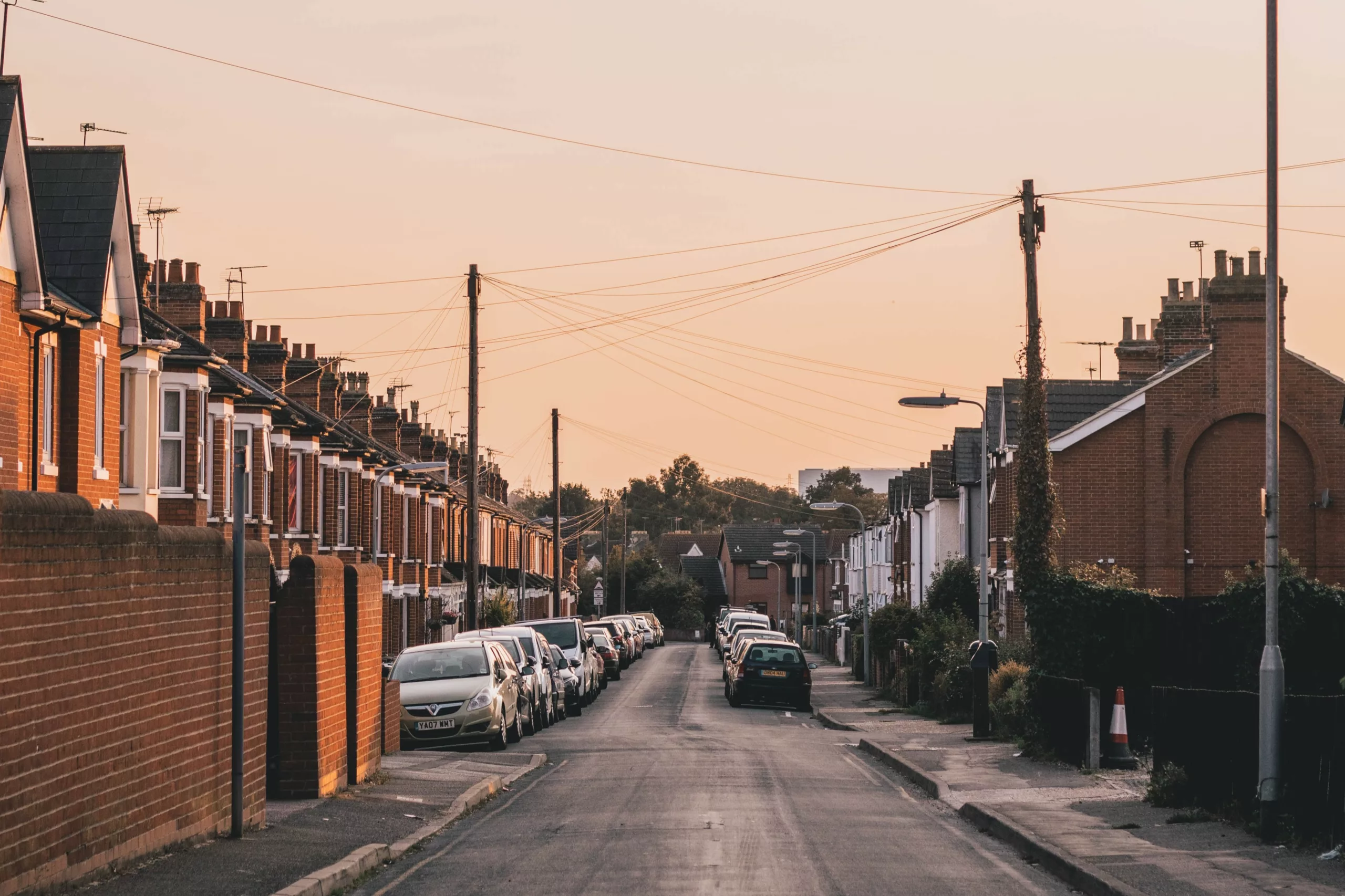 View of a street with cars parked outside houses as the sun sets