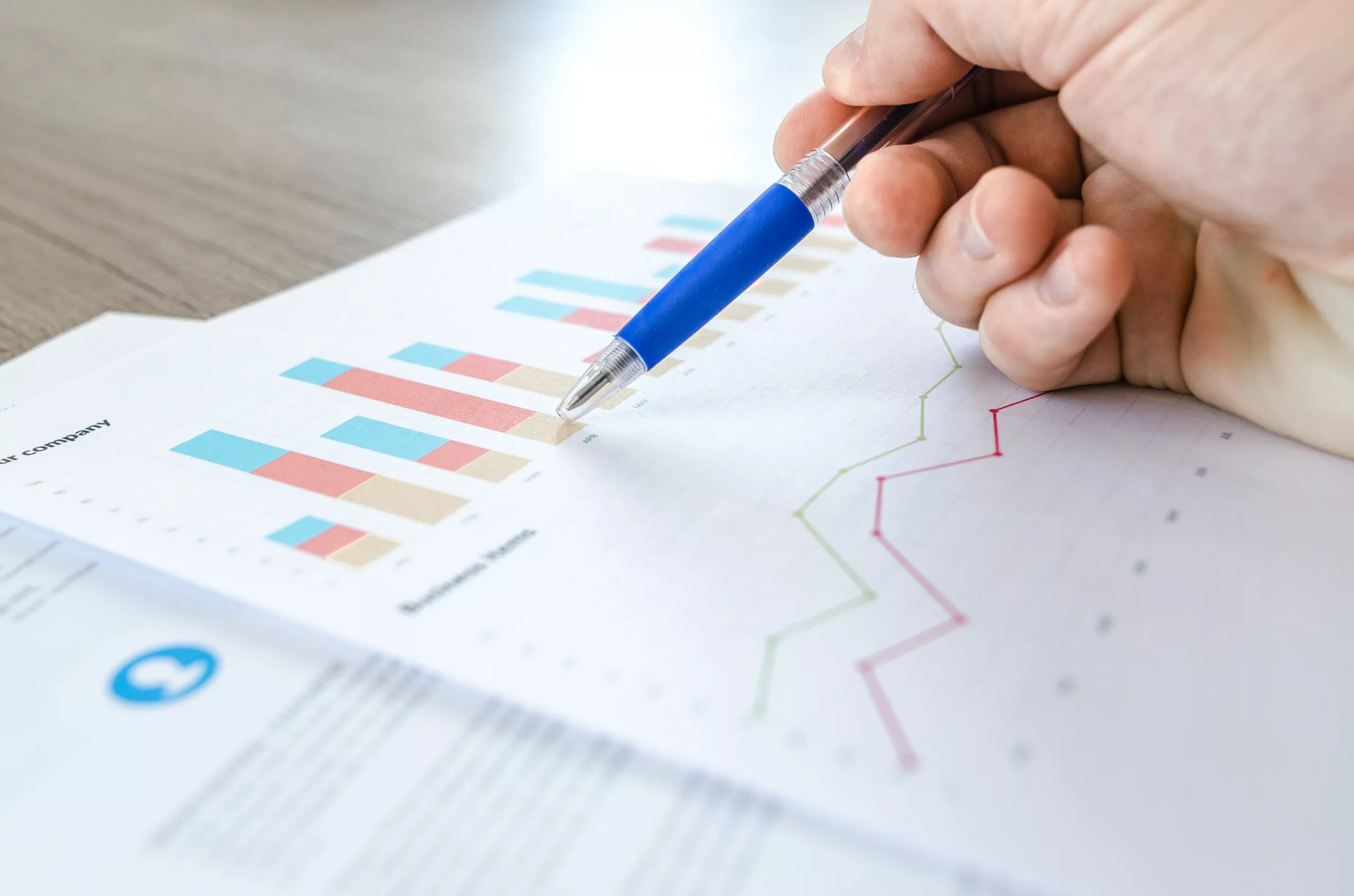 A hand holding a pen touching papers with graphs and data