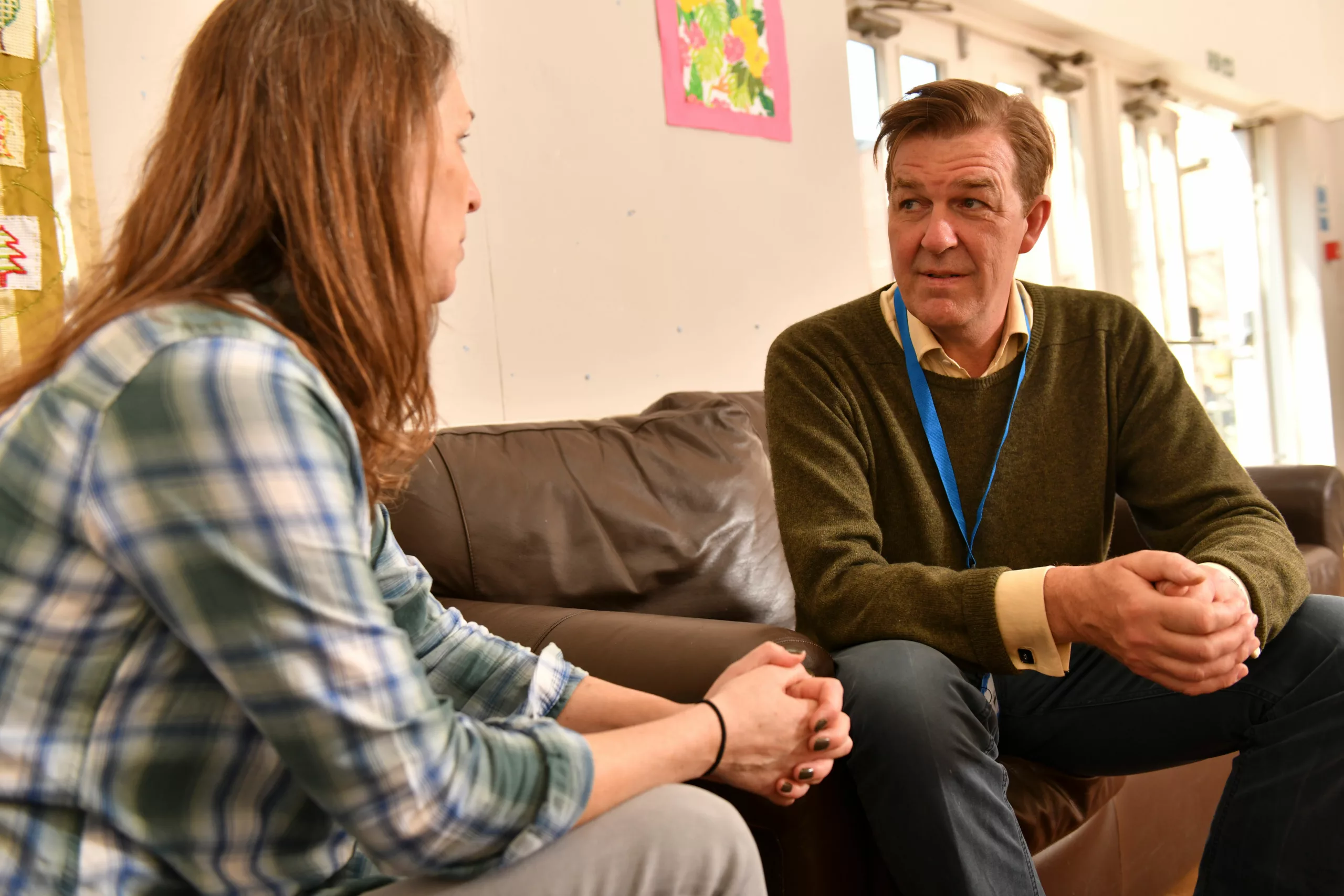 A male professional speaks to a woman sat on a sofa in a home