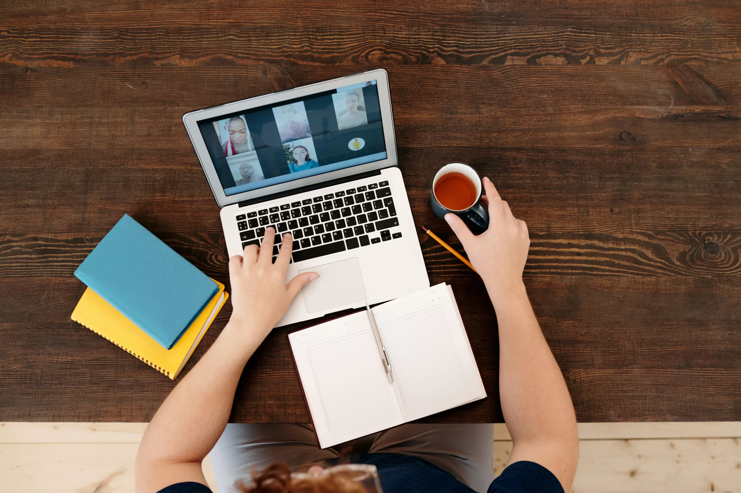 An aerial image of a person on a video call on a laptop, on a deck, with 3 pads and holding a cup of tea