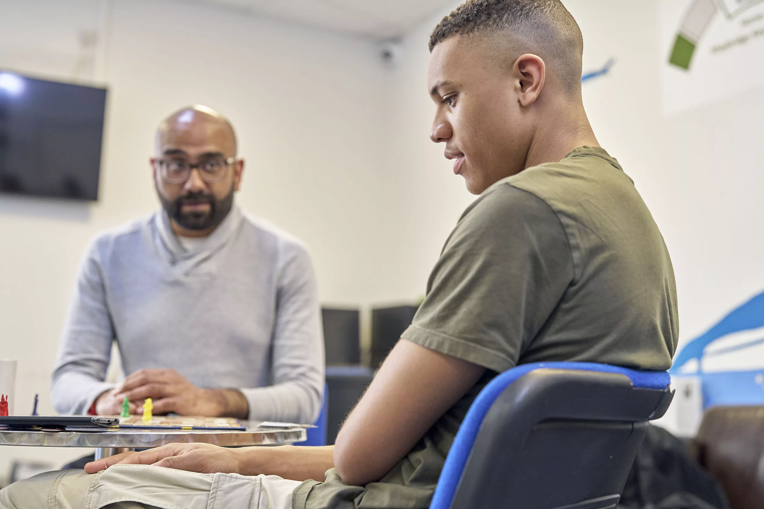 A teenage boy sits playing a gay with a male professional in a youth club setting