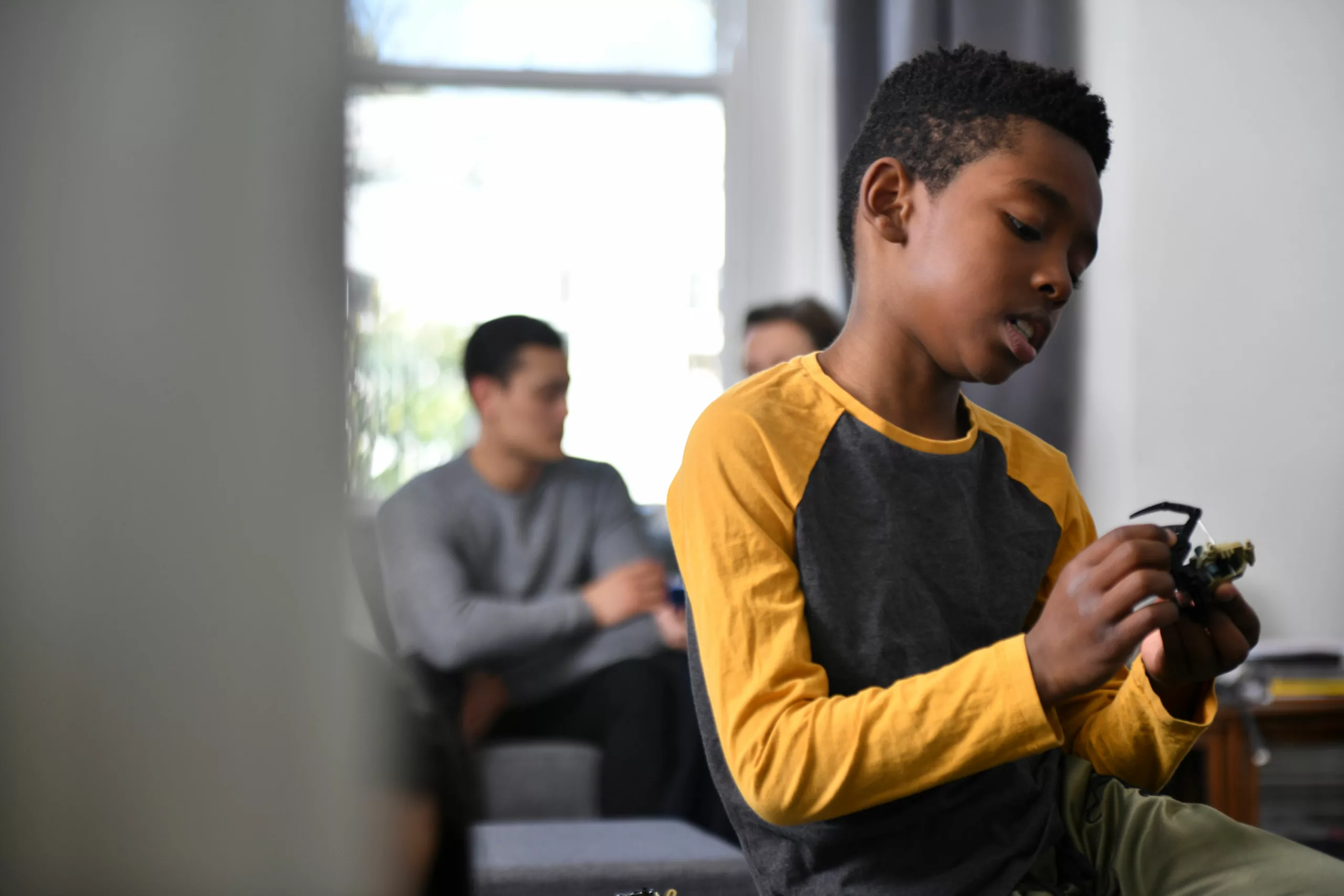 A boy plays with a toy, whilst a man and woman chat on the sofa behind him