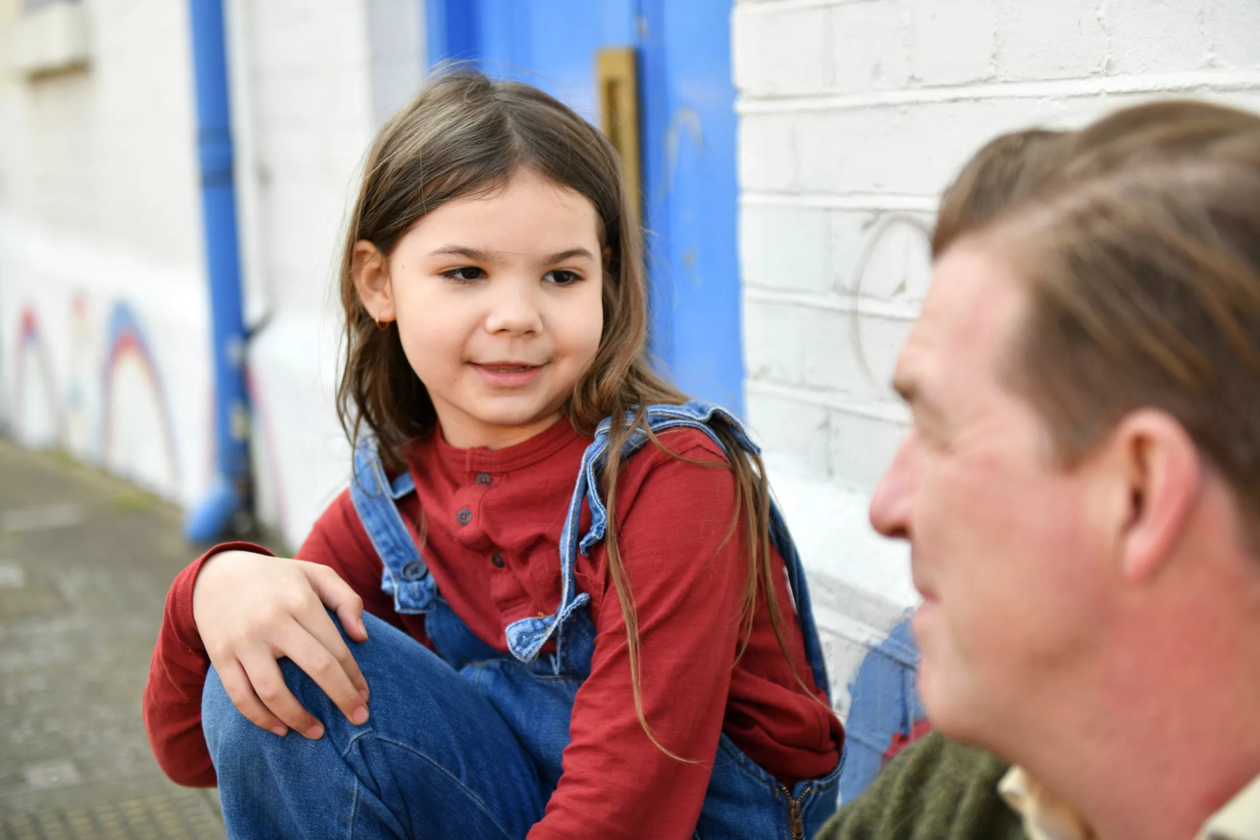 A young girl looks at a male professional as they sit together on a wall