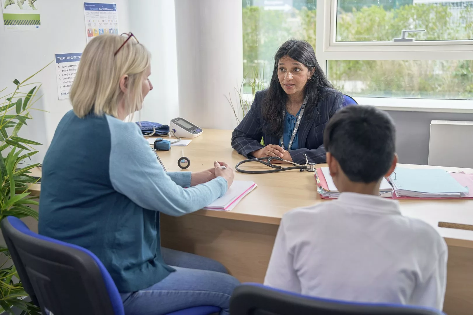 Female professional, young boy and GP around a desk chatting in a health setting