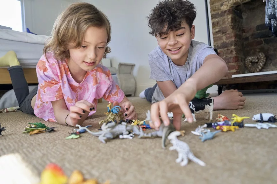 Brother and sister lying on floor playing with plastic animals