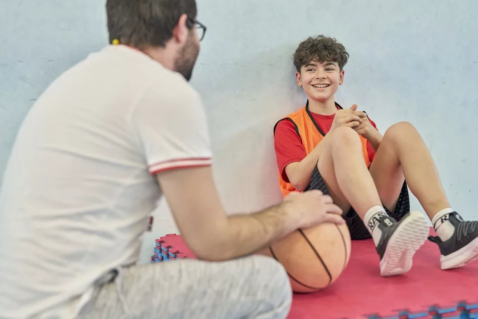 Sports coach speaks to young boy in a sports hall