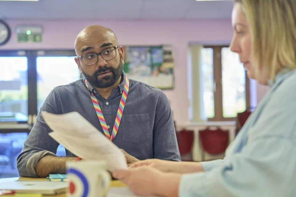 A male and female professional having a conversation around a desk with paperwork