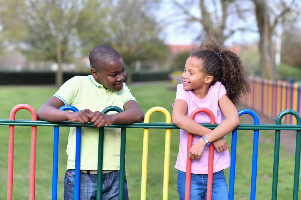 A young boy and girl at a gate in the park