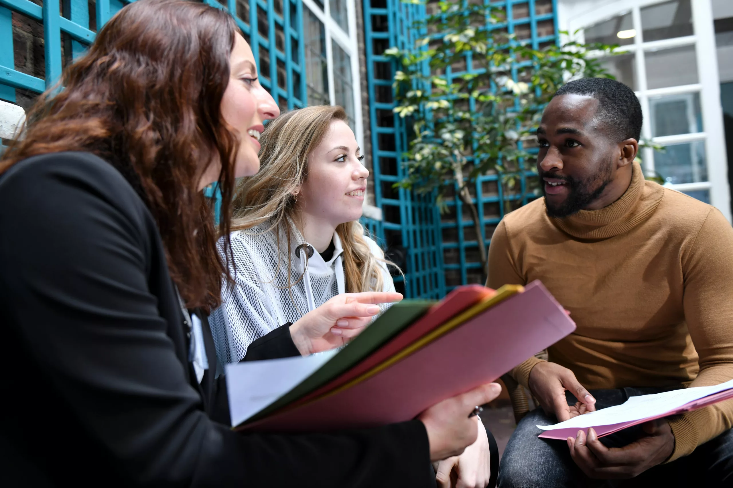 Two professionals and a young person chatting over a report in a garden