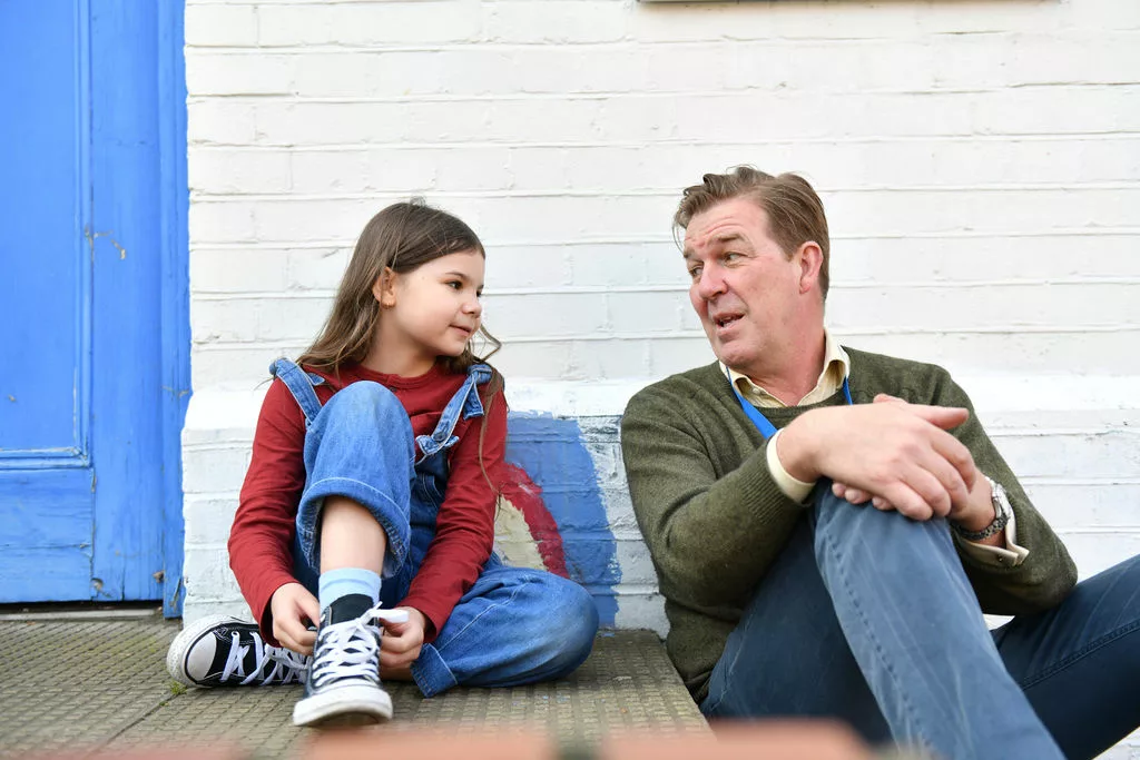 Young girl sat side-by-side on the ground with a male professional chatting