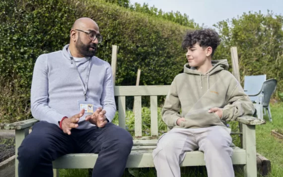 Male professional speak to a boy on a bench in a garden setting