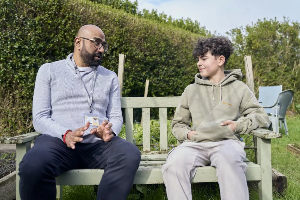 Male professional speak to a boy on a bench in a garden setting