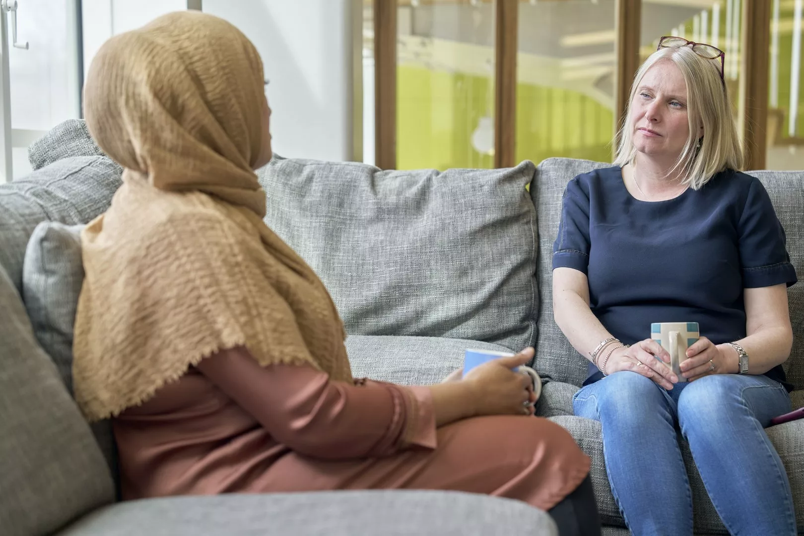 Two women sat on the sofa chatting with mugs