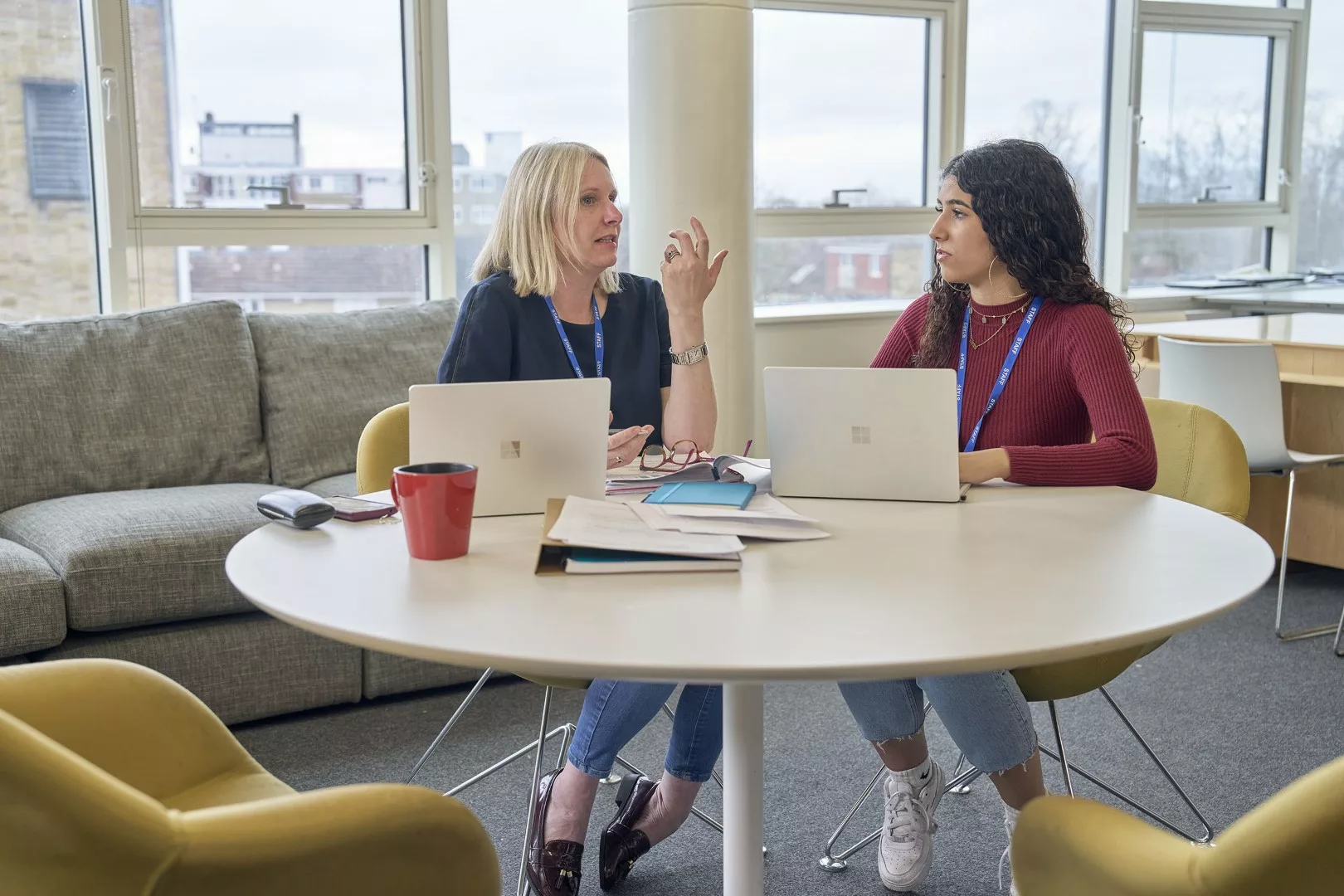 Two female professionals in a staff room chatting over a table