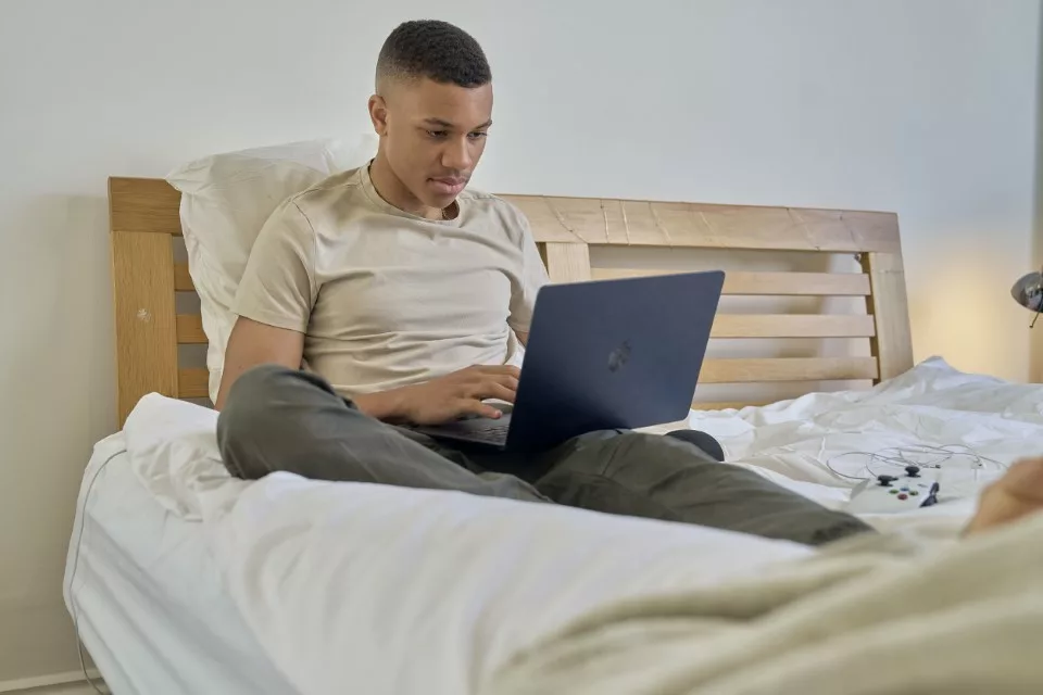 Teenage boy on laptop on his bed, looking worried