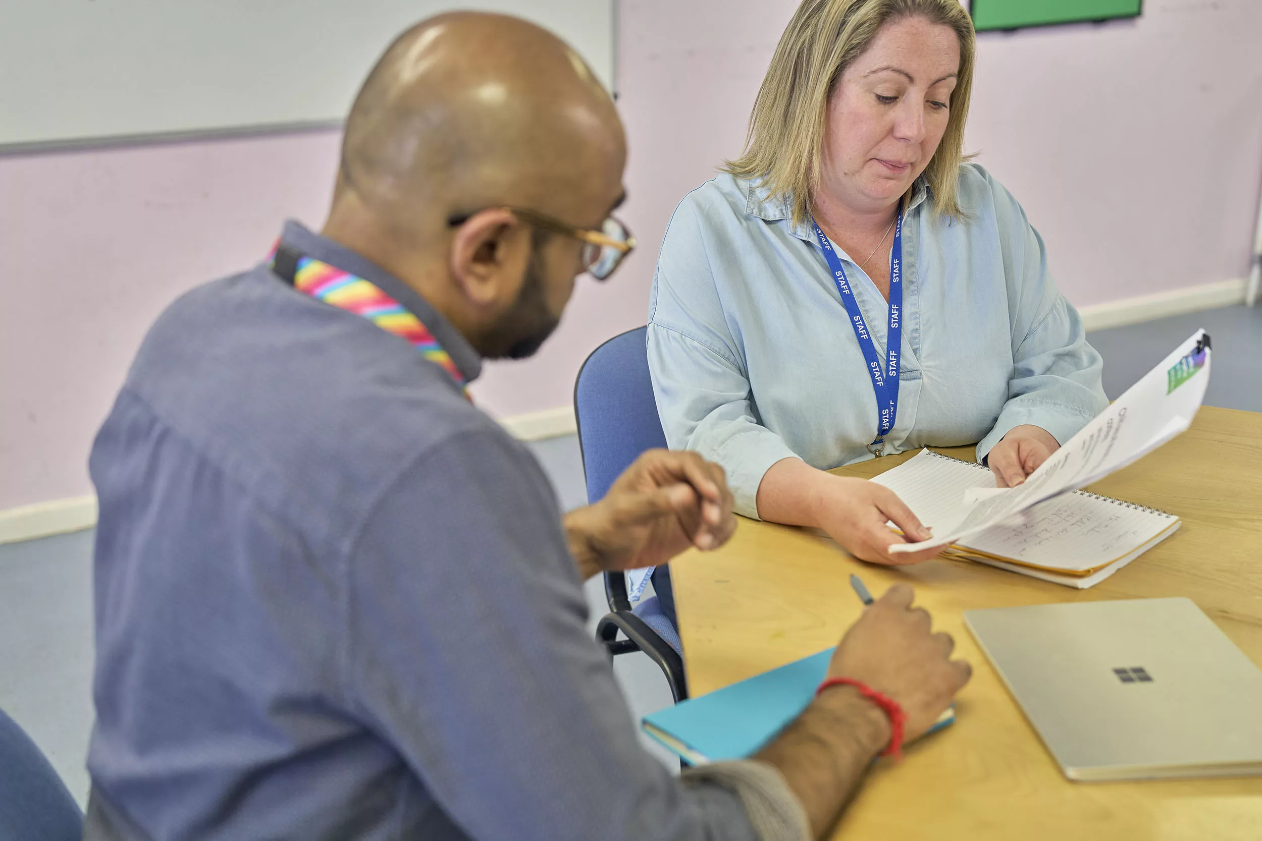 A male and female professional look at a document together sat around a desk