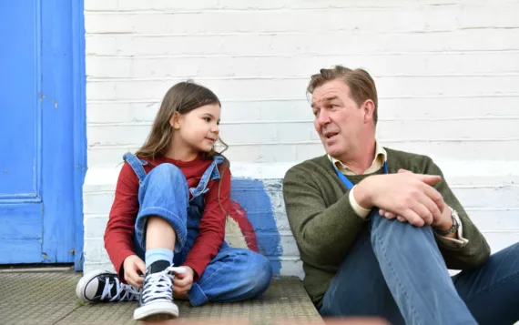 Professional speaking to child on the steps of a youth club