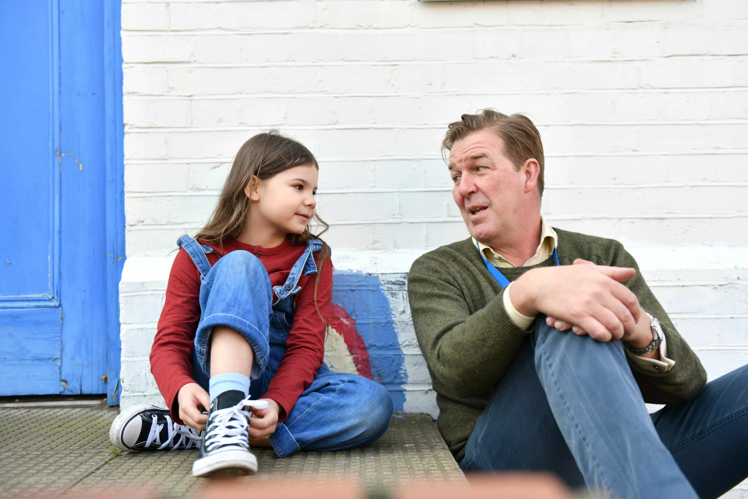 Professional speaking to child on the steps of a youth club