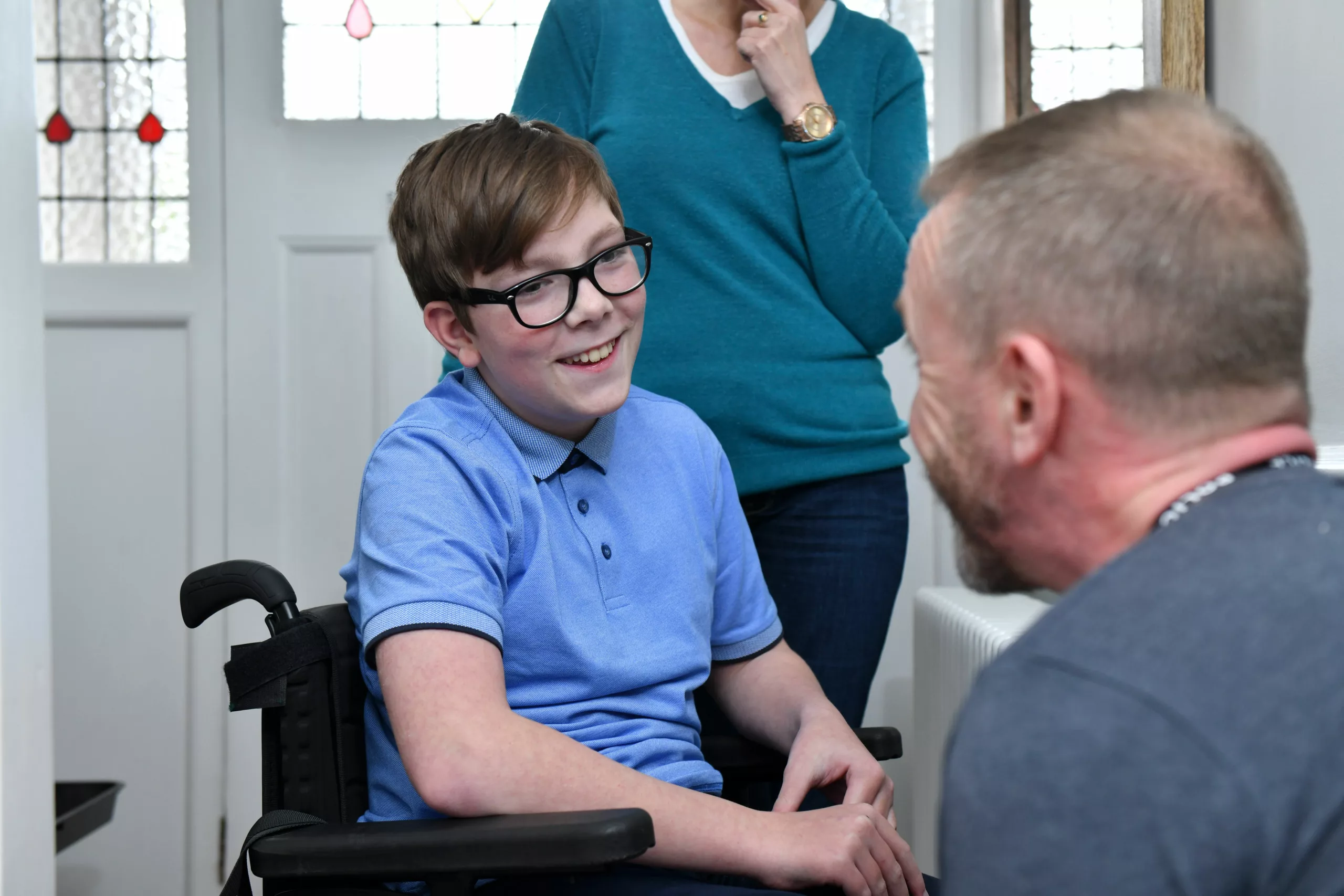 Boy in a wheelchair speaking to a professional in a hallway at home