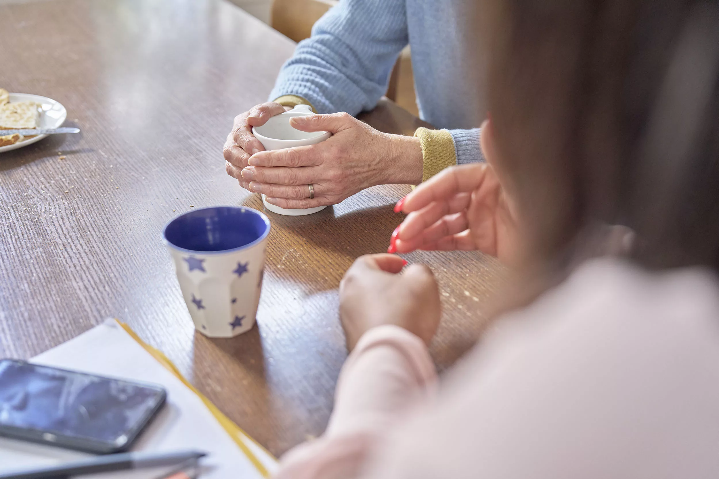 The hands of a mother and a social worker holding cups of tea at a kitchen table