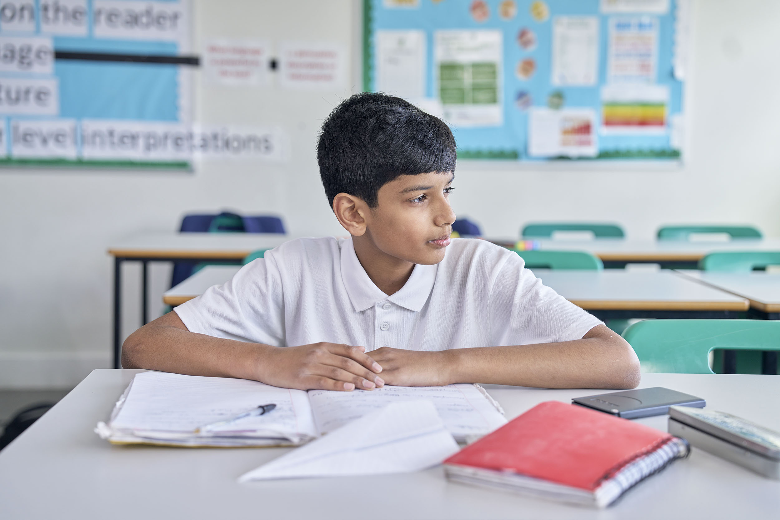 School boy sat at desk in classroom looking out of window to his left