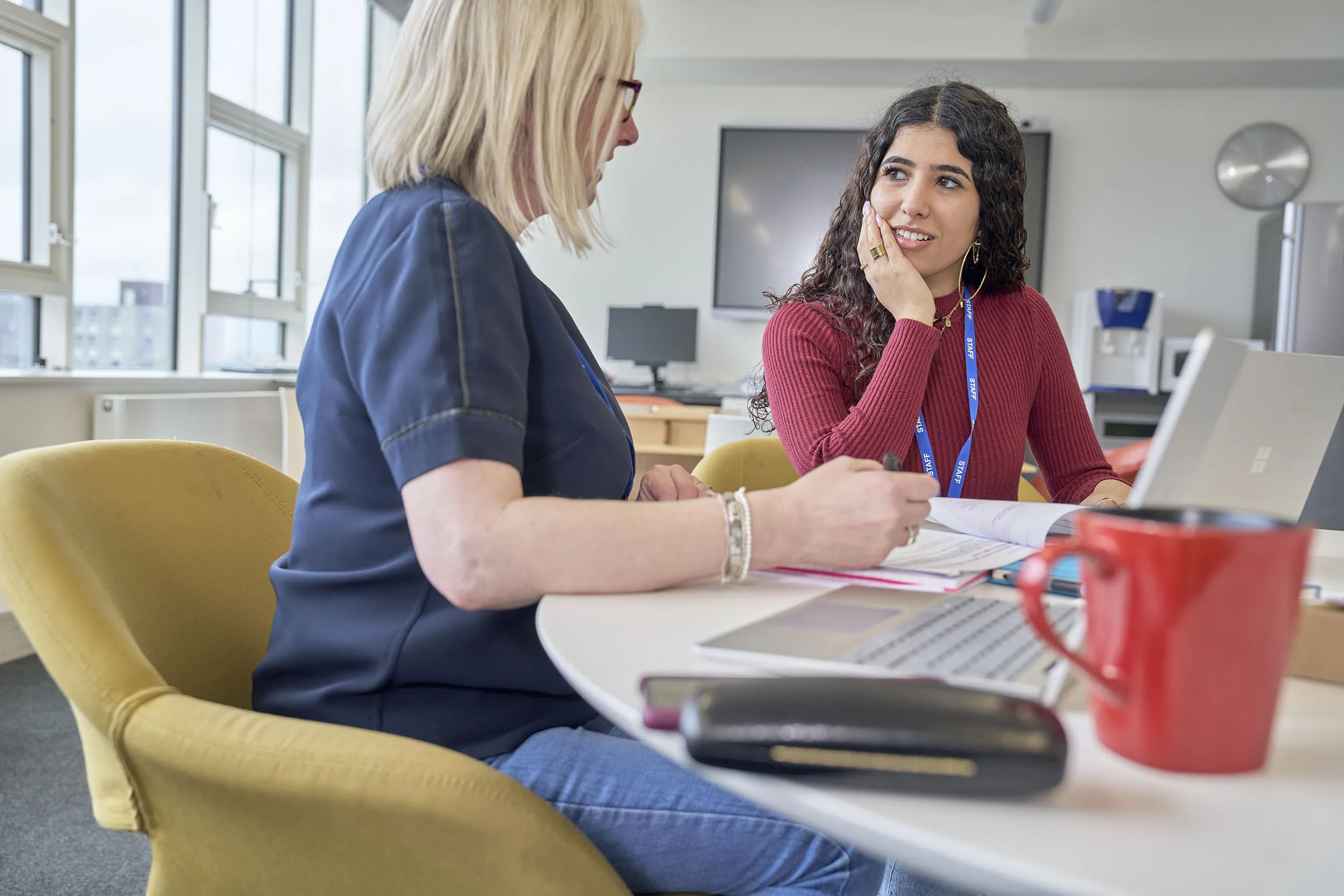 Two professionals sat at a table discussing work together in a staff room