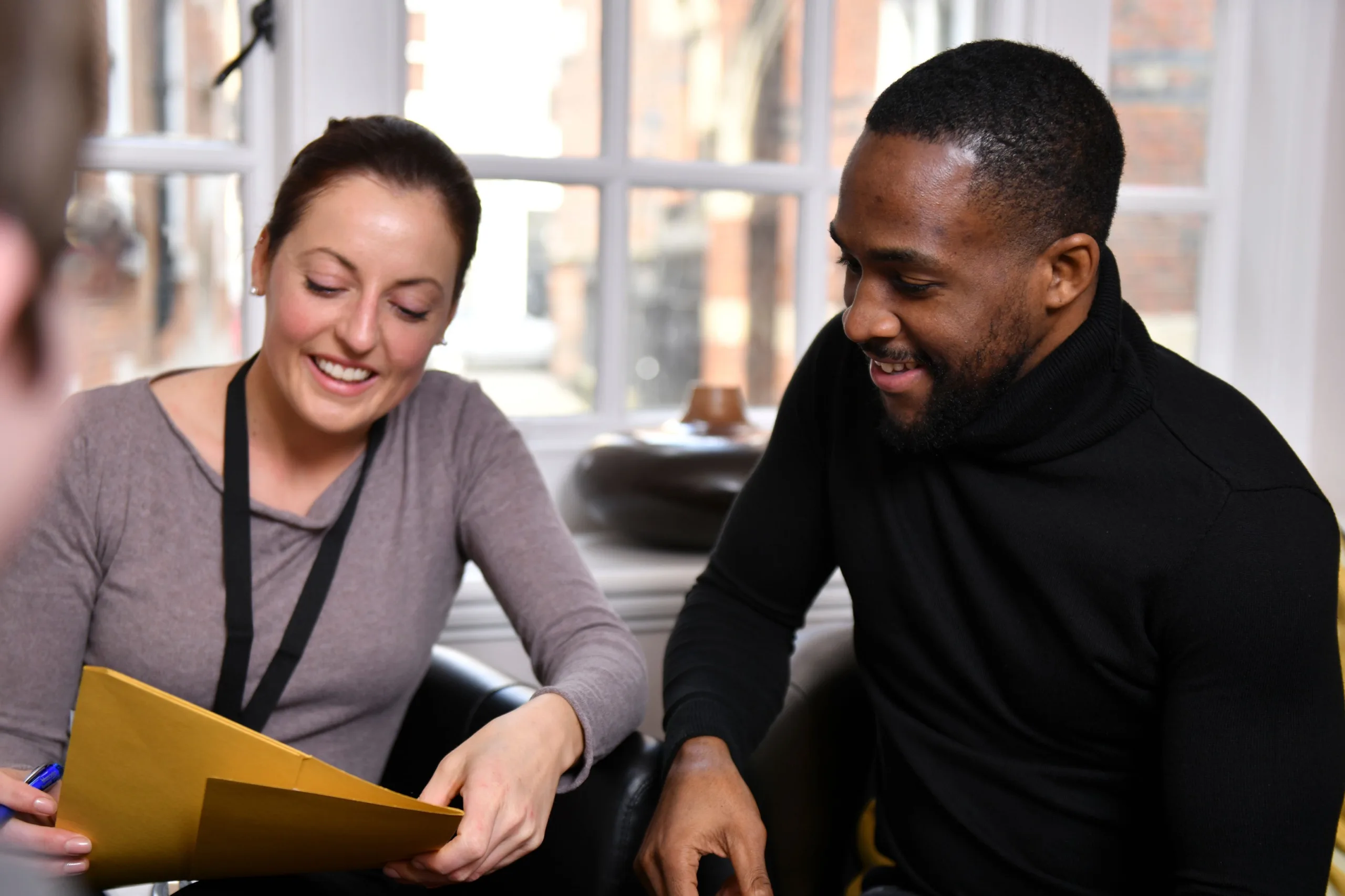 A male and a female professional smiling, looking at printed pieces of work in a folder