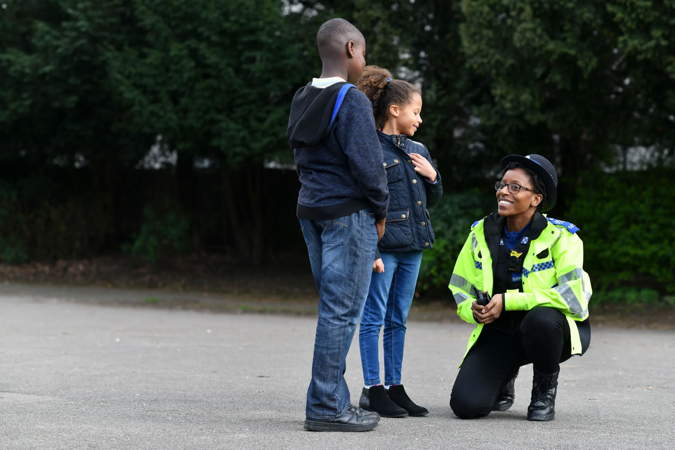 Community Support Officer kneeling down to speak to two children in a park