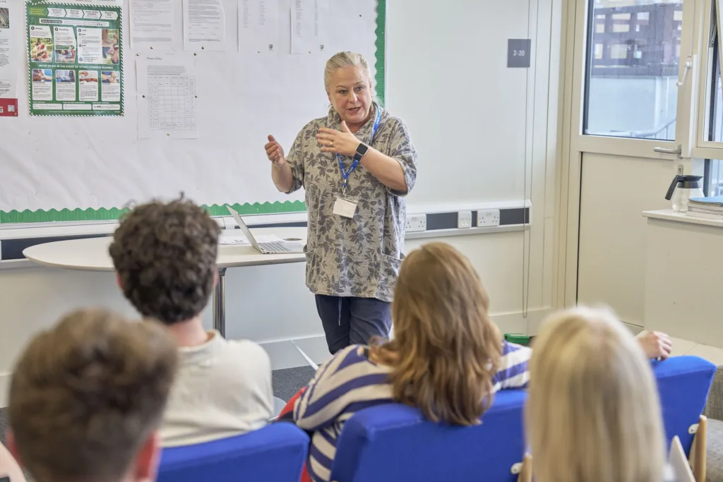Professional leading a presentation in front of seated colleagues in a bright staff room