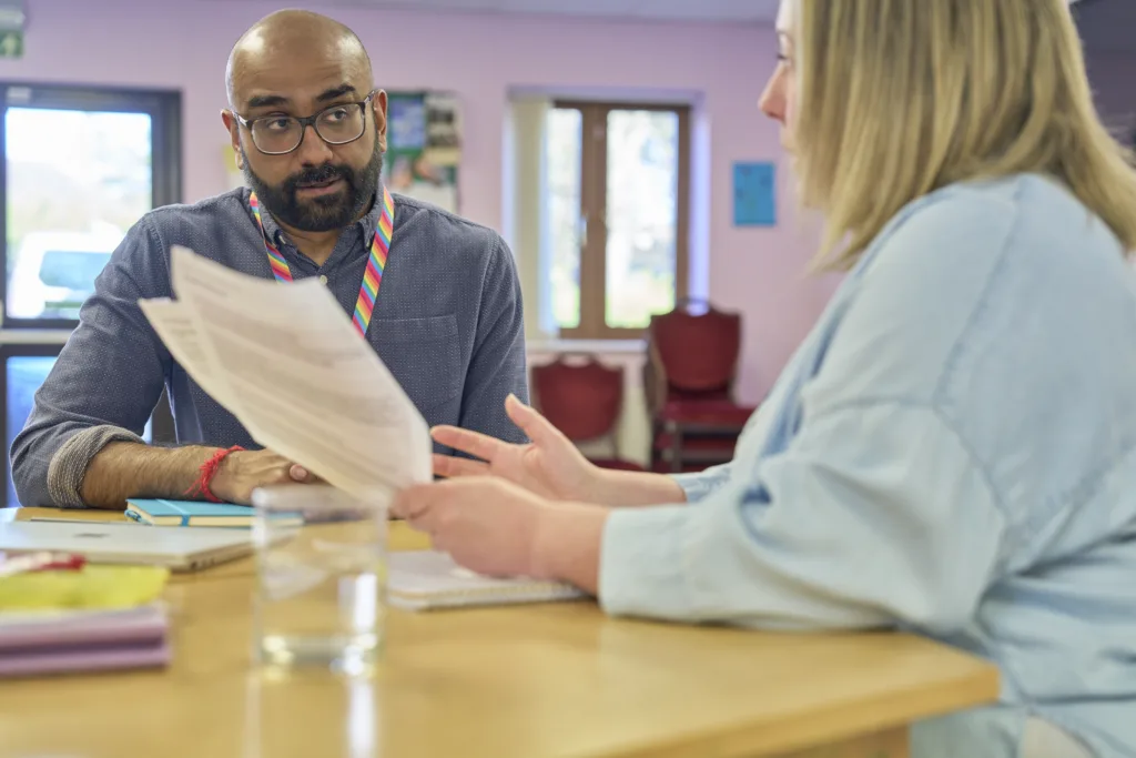 One male and one female professional discussing data gathered during audit, sat at table in staff room